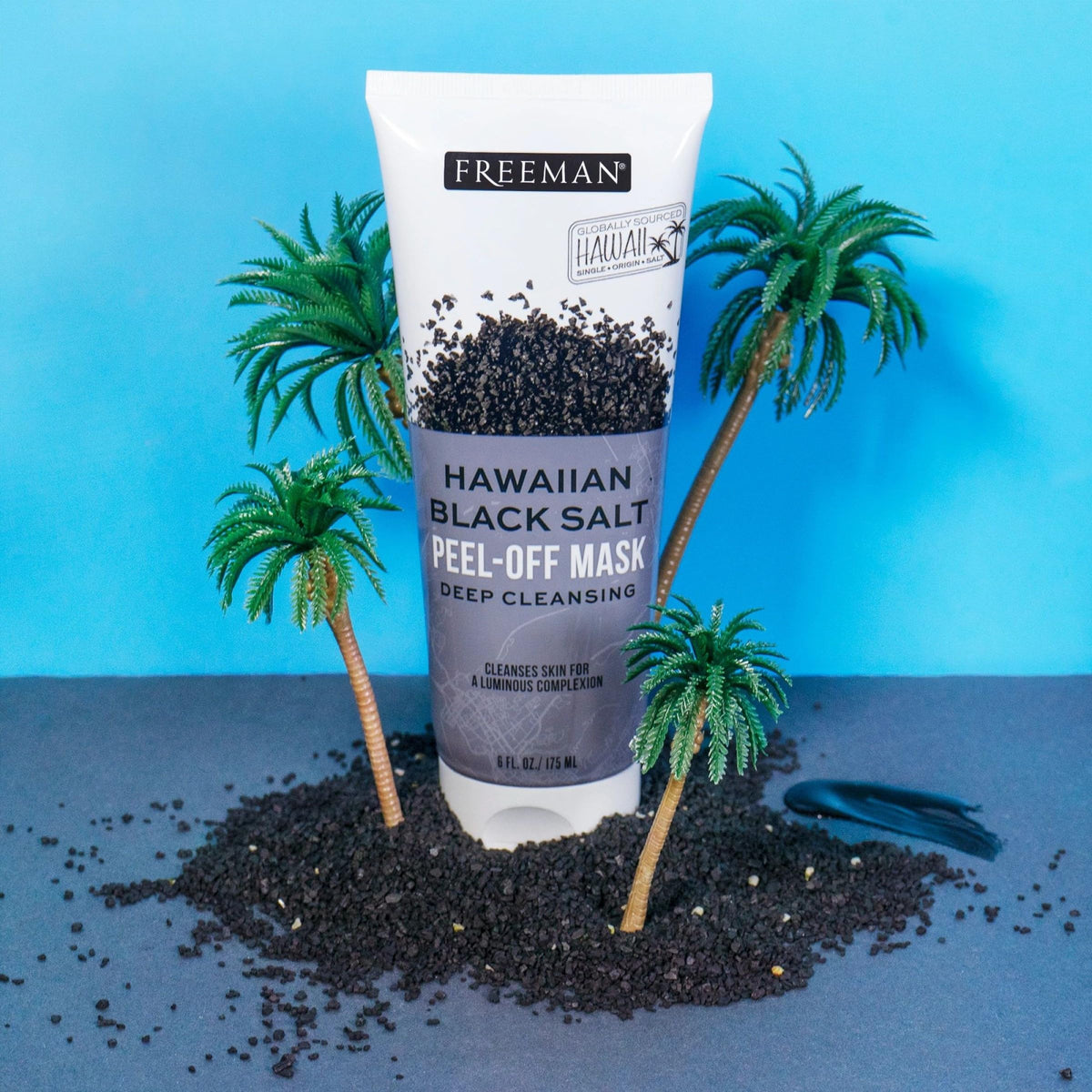 Mask tube standing in black salt crystals among small toy palm trees on blue