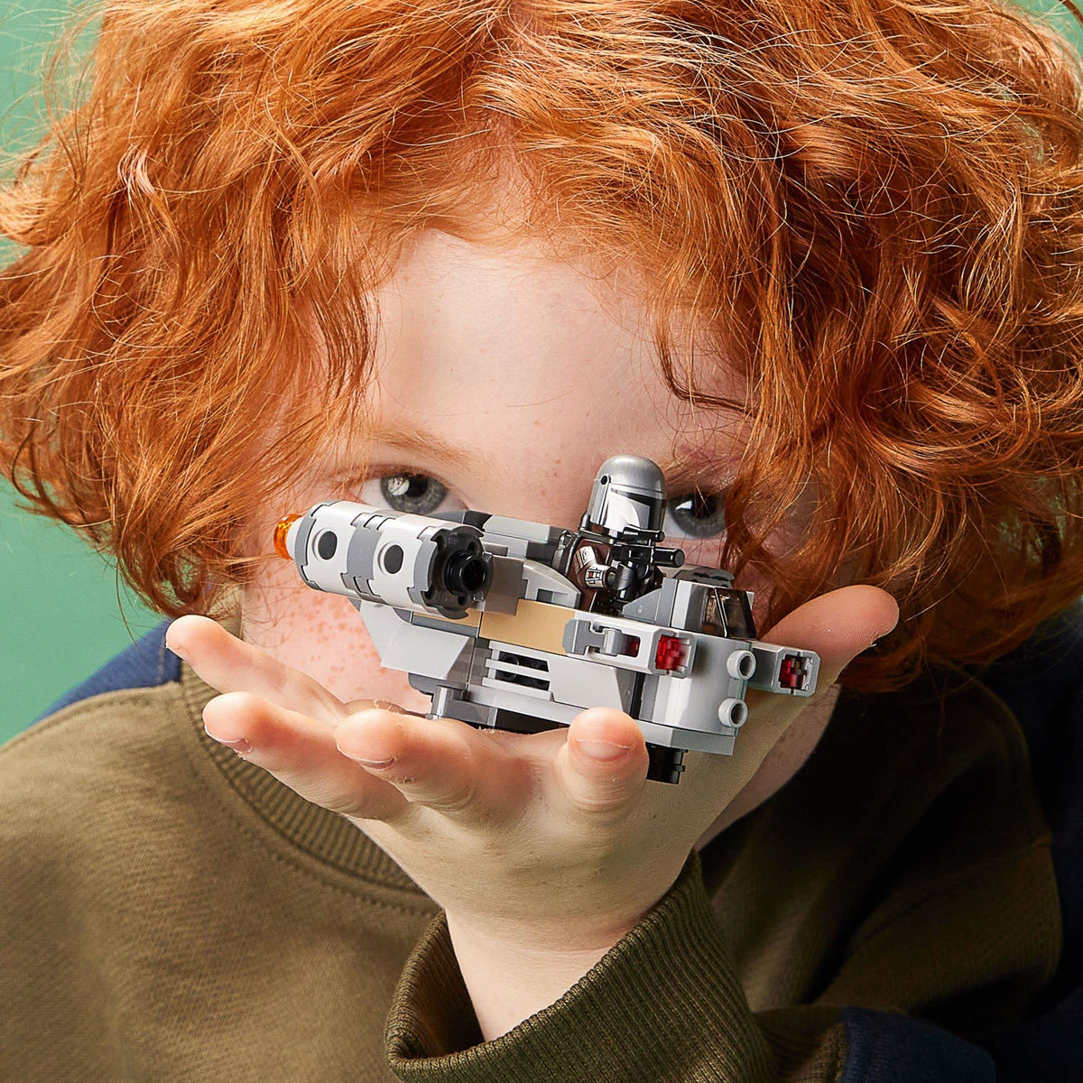 Red-haired child peeking over the Razor Crest microfighter held in an open hand