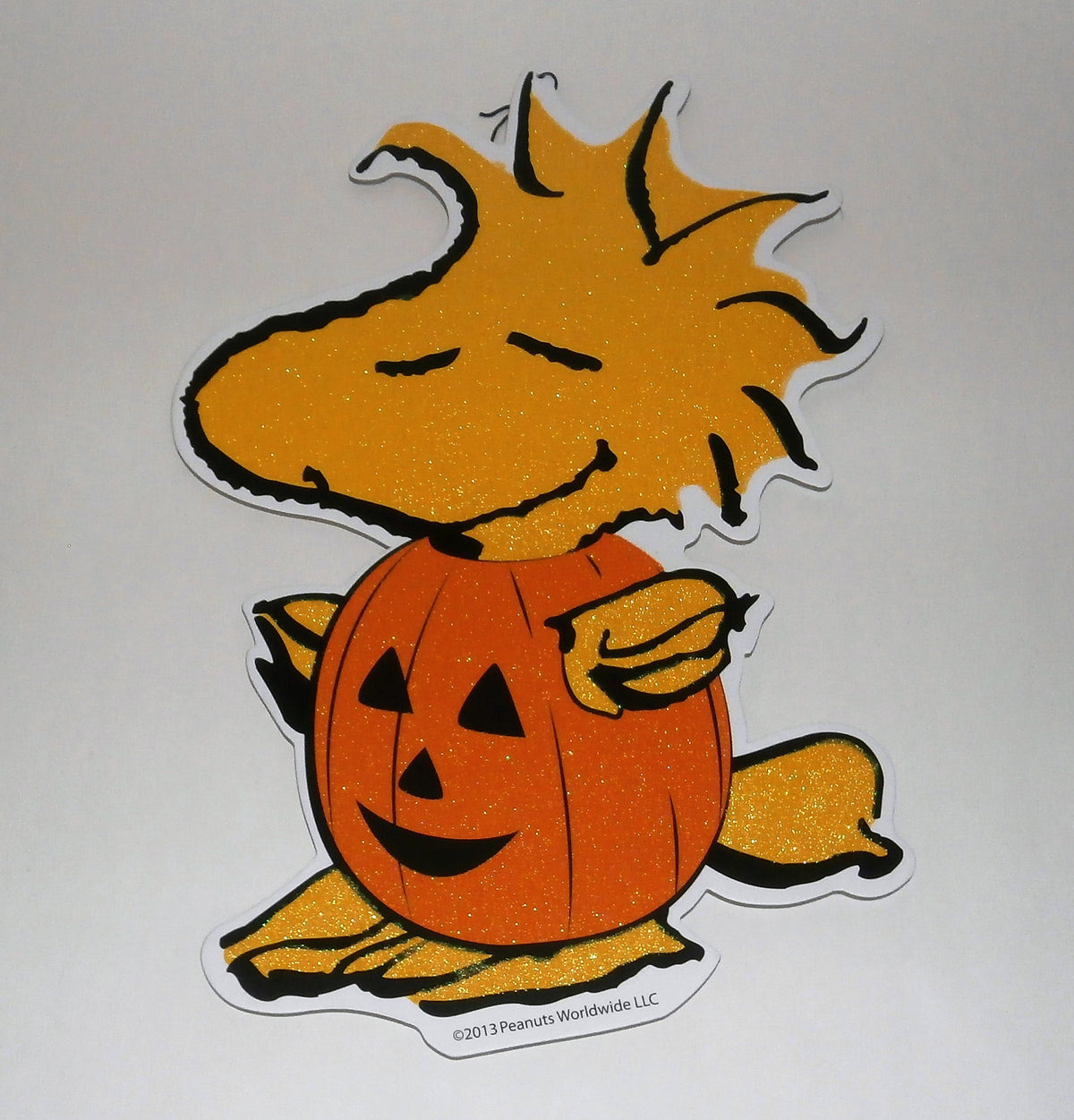 Glittery die-cut wall sign of Woodstock wearing a smiling jack-o-lantern costume