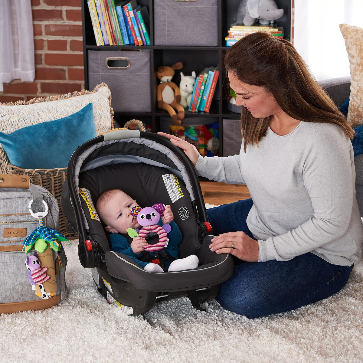 Baby in a car seat holding a purple Lamaze koala rattle while a parent looks on