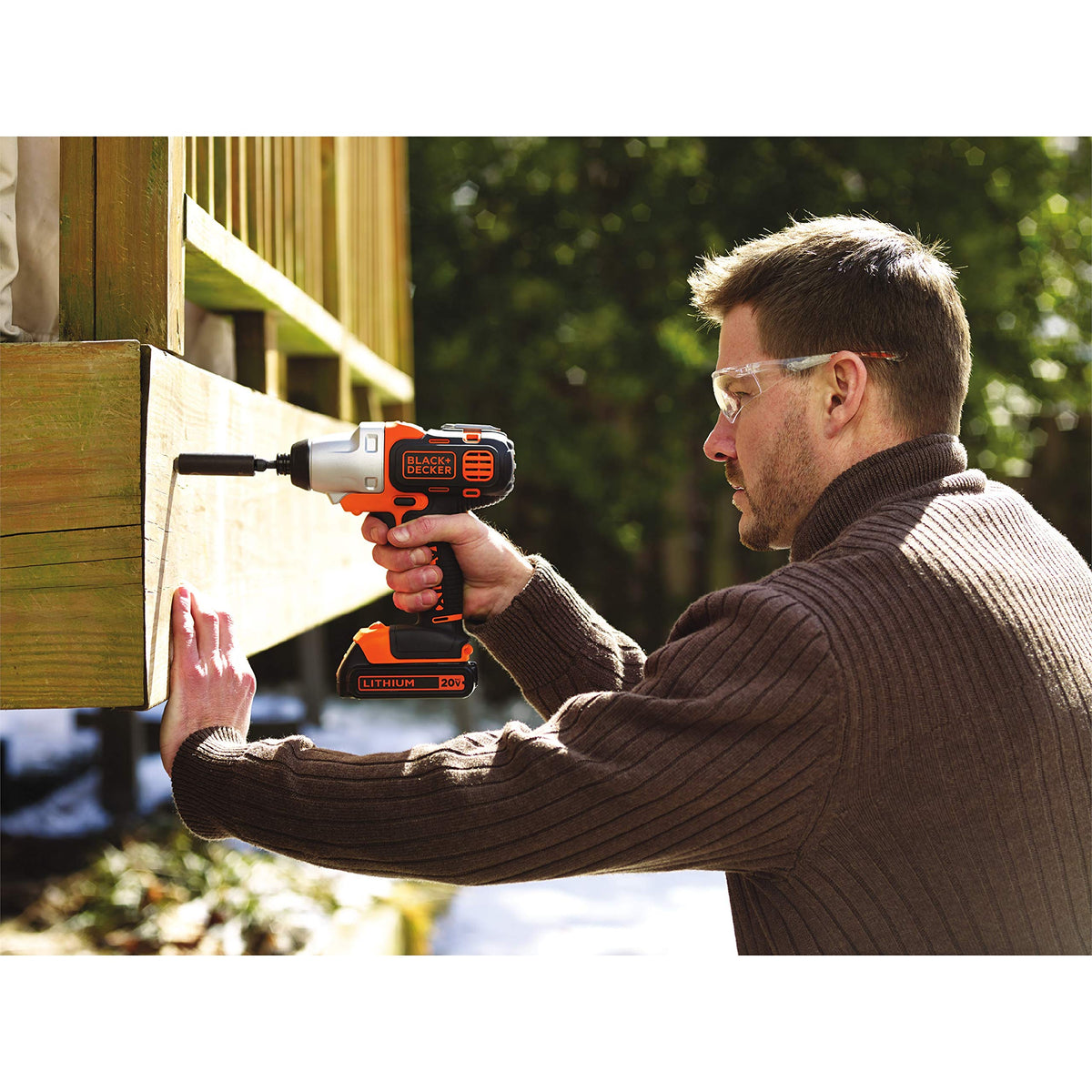Man driving a bolt into an outdoor deck beam with an orange 20V impact driver