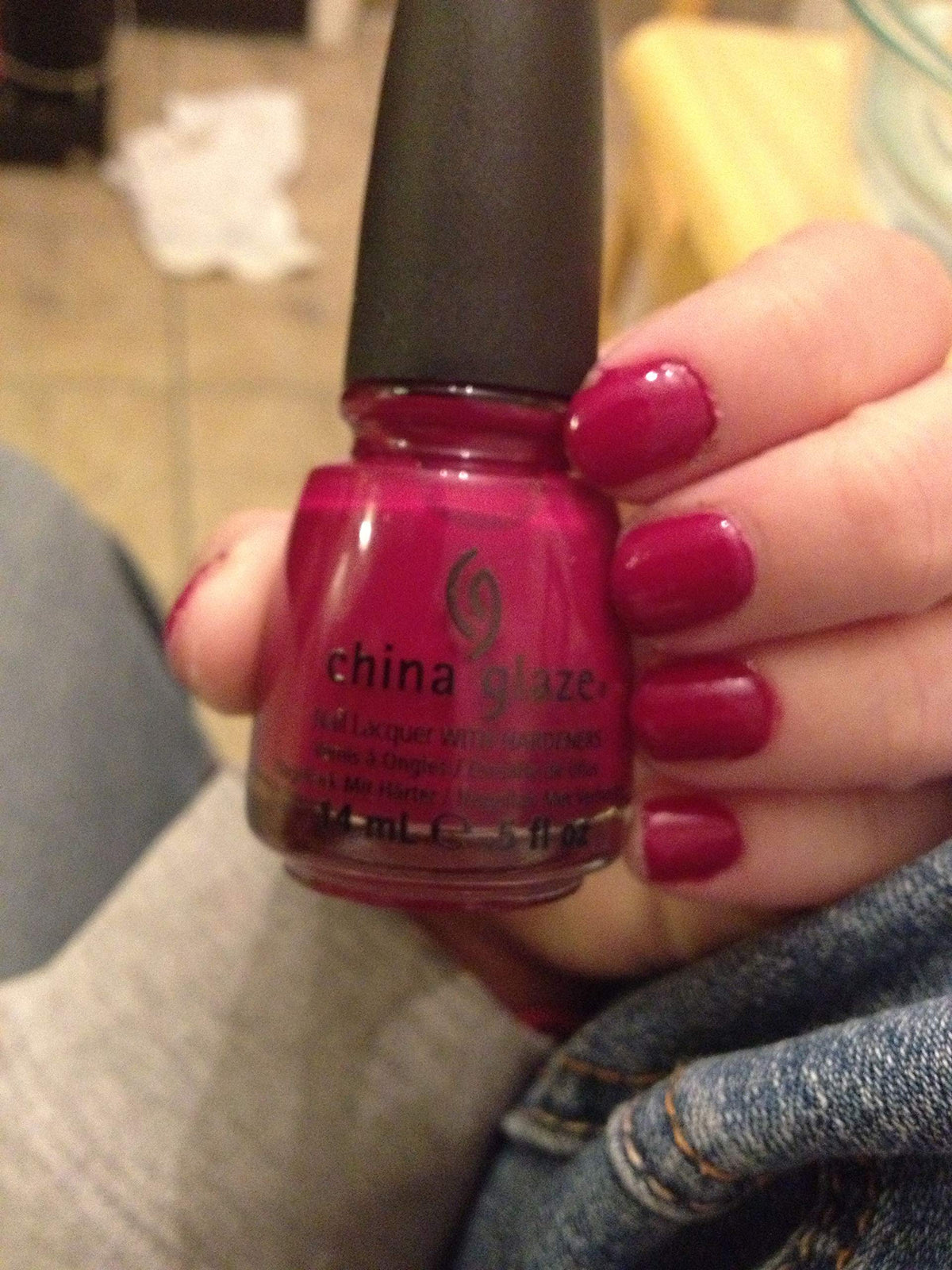Hand holding a raspberry red polish bottle with matching painted nails