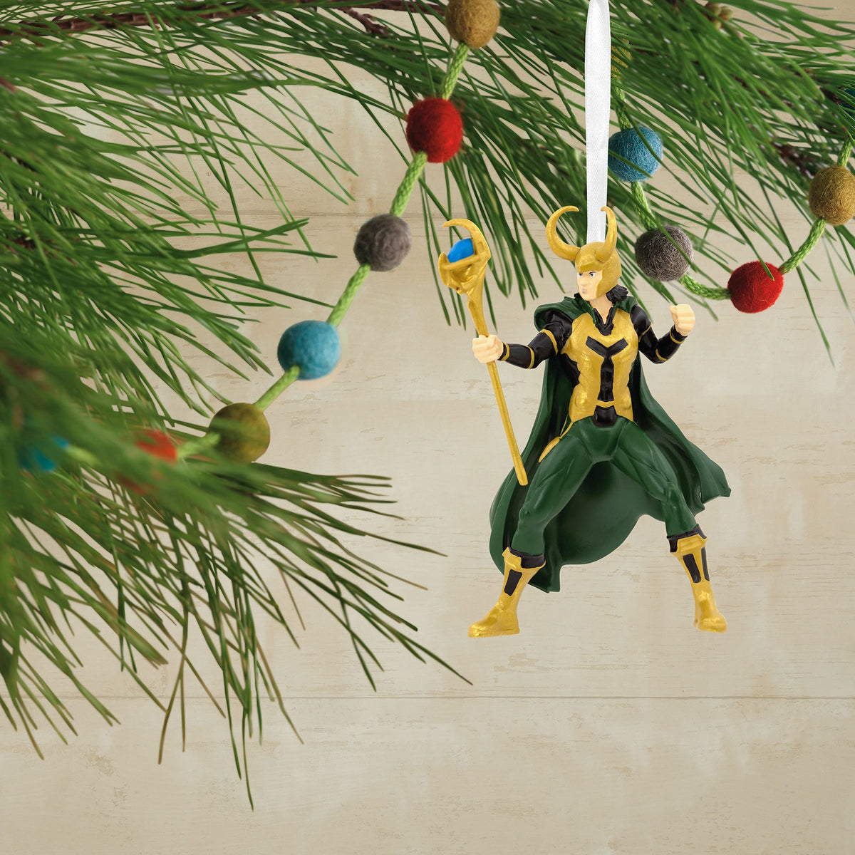Horned-helmet figure ornament hanging on a pine branch with a felt ball garland
