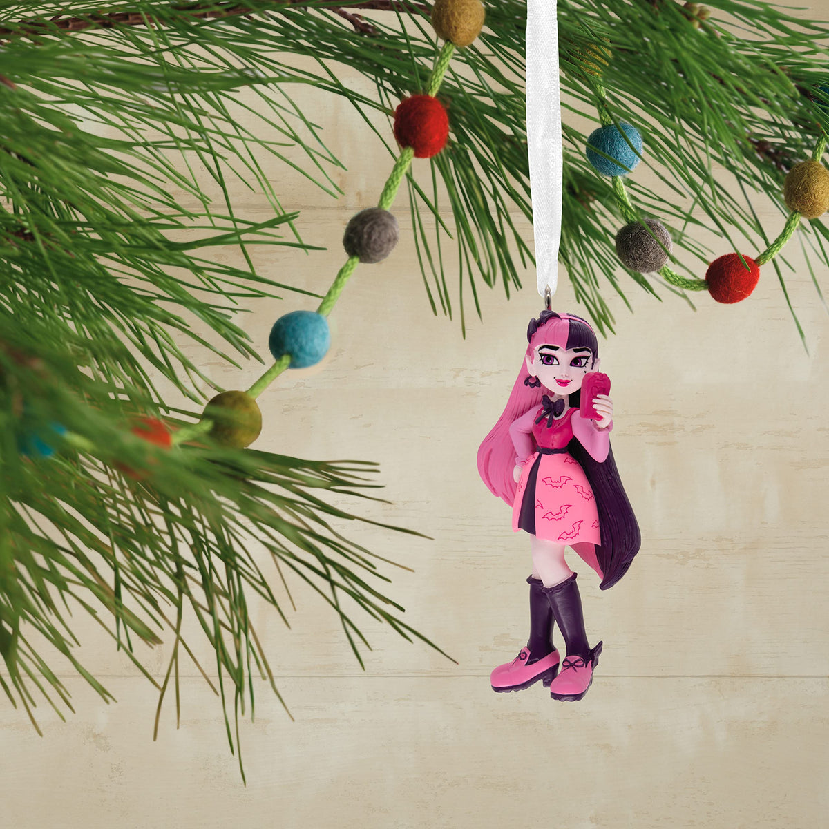 Vampire girl ornament hanging on a pine branch with a felt ball garland