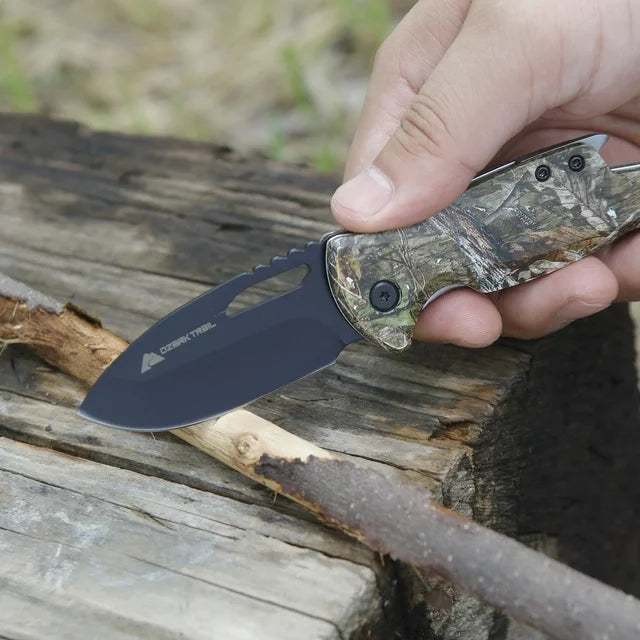 Hand whittling a stick on a log with the black-bladed camo knife