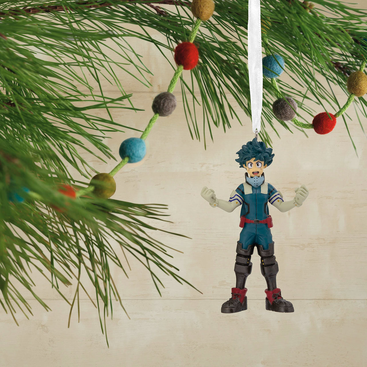 Green-haired hero ornament hanging on a pine branch with a felt ball garland