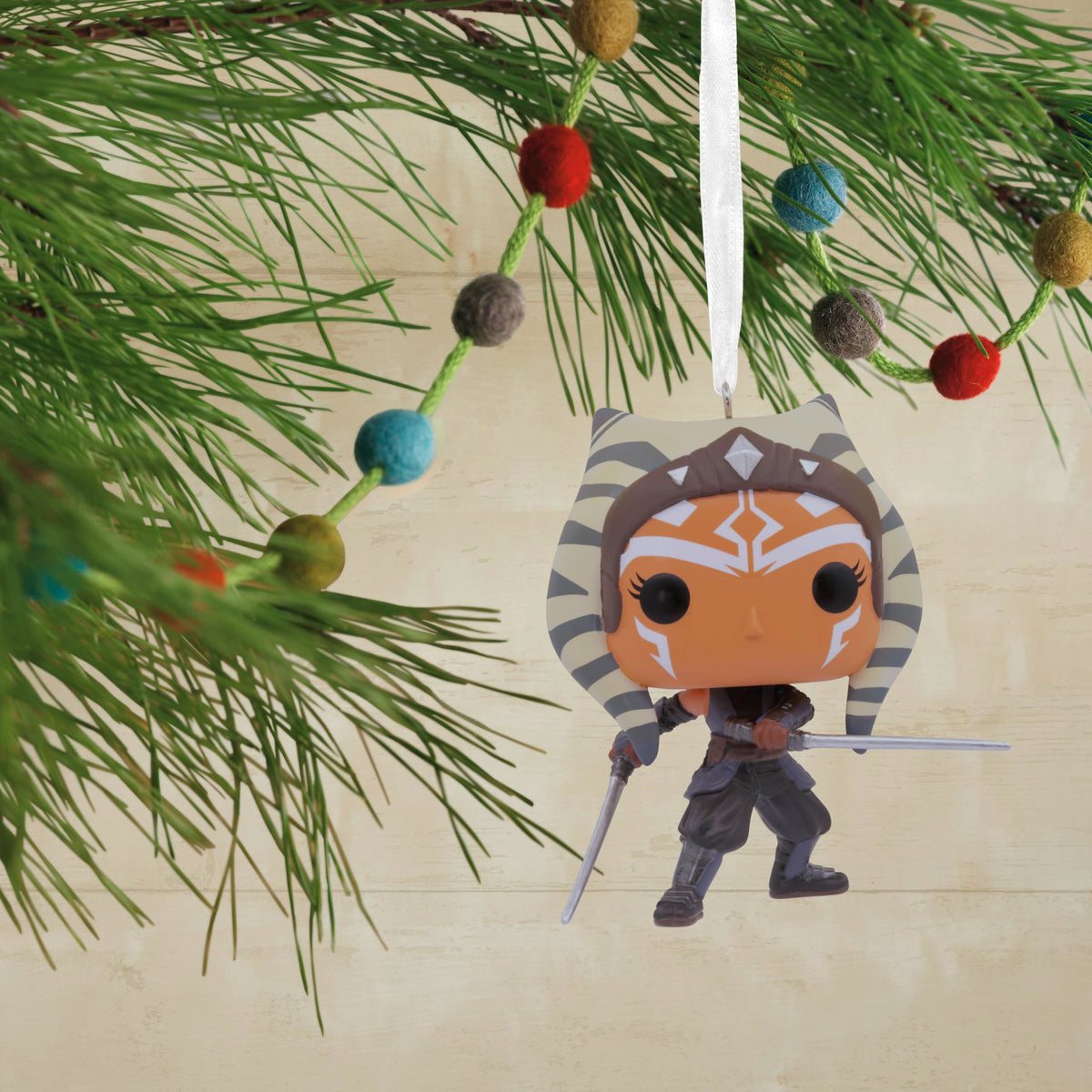 Twin-blade warrior vinyl ornament hanging on a pine branch with a felt ball garland