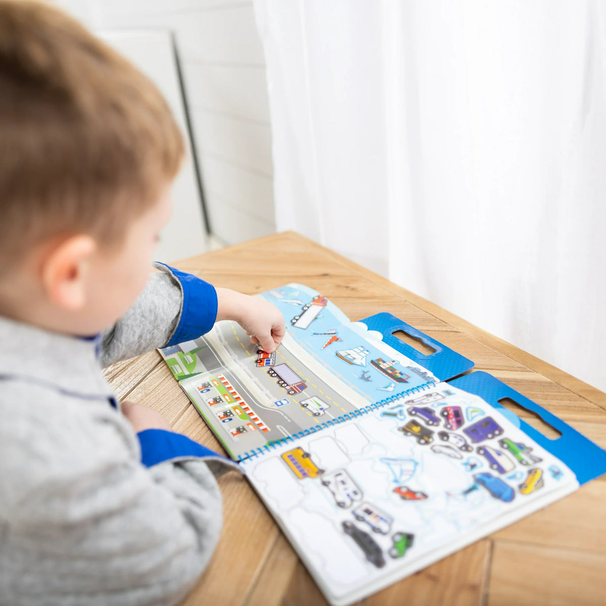Boy at a table adding vehicle stickers to the open highway and harbor scene