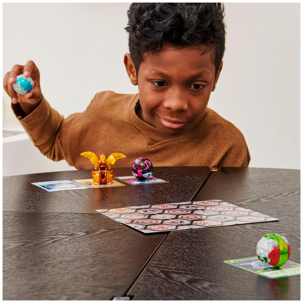 Boy holding a Bakugan ball ready to roll toward a hex-pattern game mat
