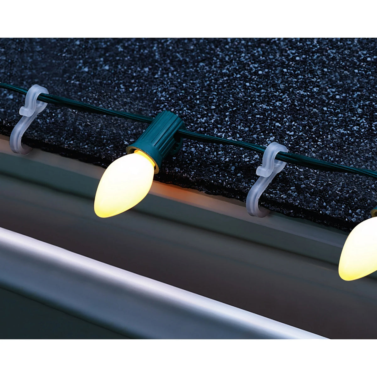 Close-up of clear hooks slid under roof shingles holding warm white C9 bulbs