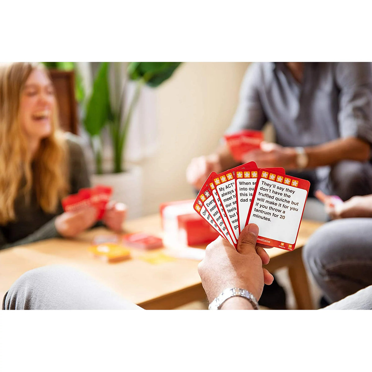 Player holding a fan of red review cards as friends laugh at a coffee table