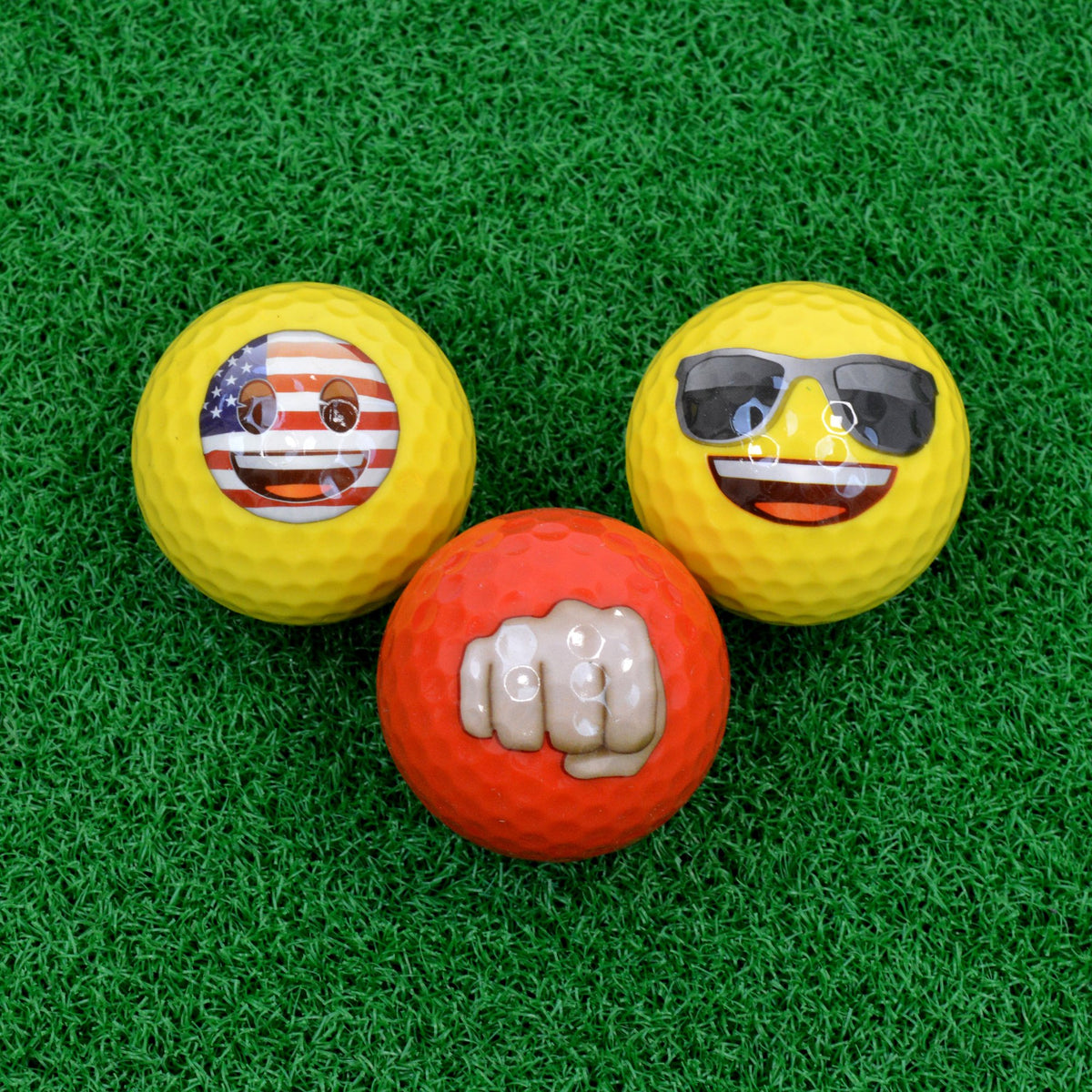 Three emoji golf balls on turf: US flag face, sunglasses face and red fist bump