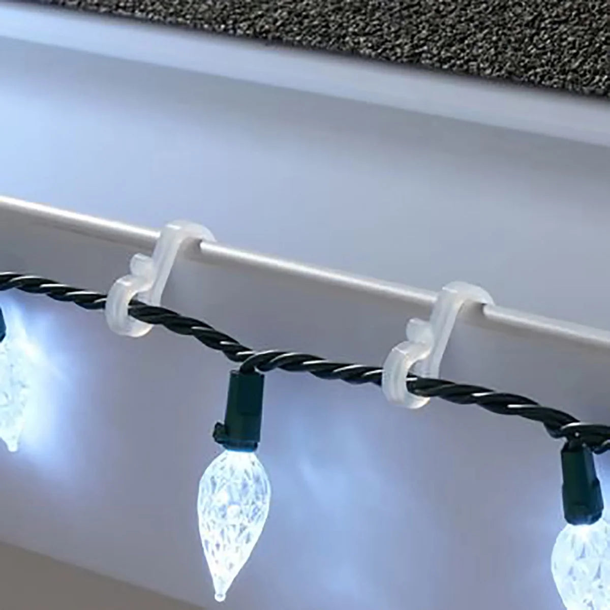 Clear hooks holding a string of white C9 LED bulbs along a white gutter