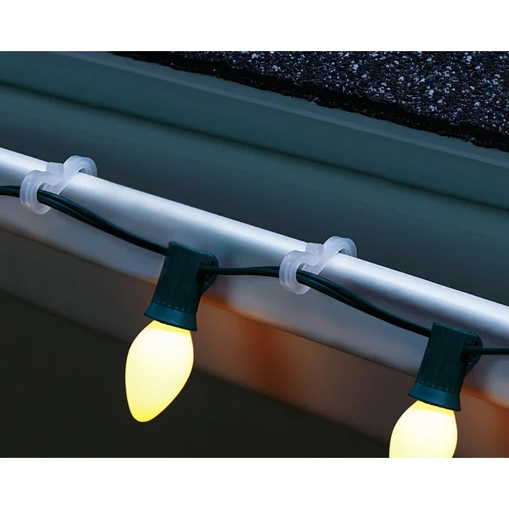 Clear hooks on a gutter edge holding glowing warm white C9 bulbs at dusk