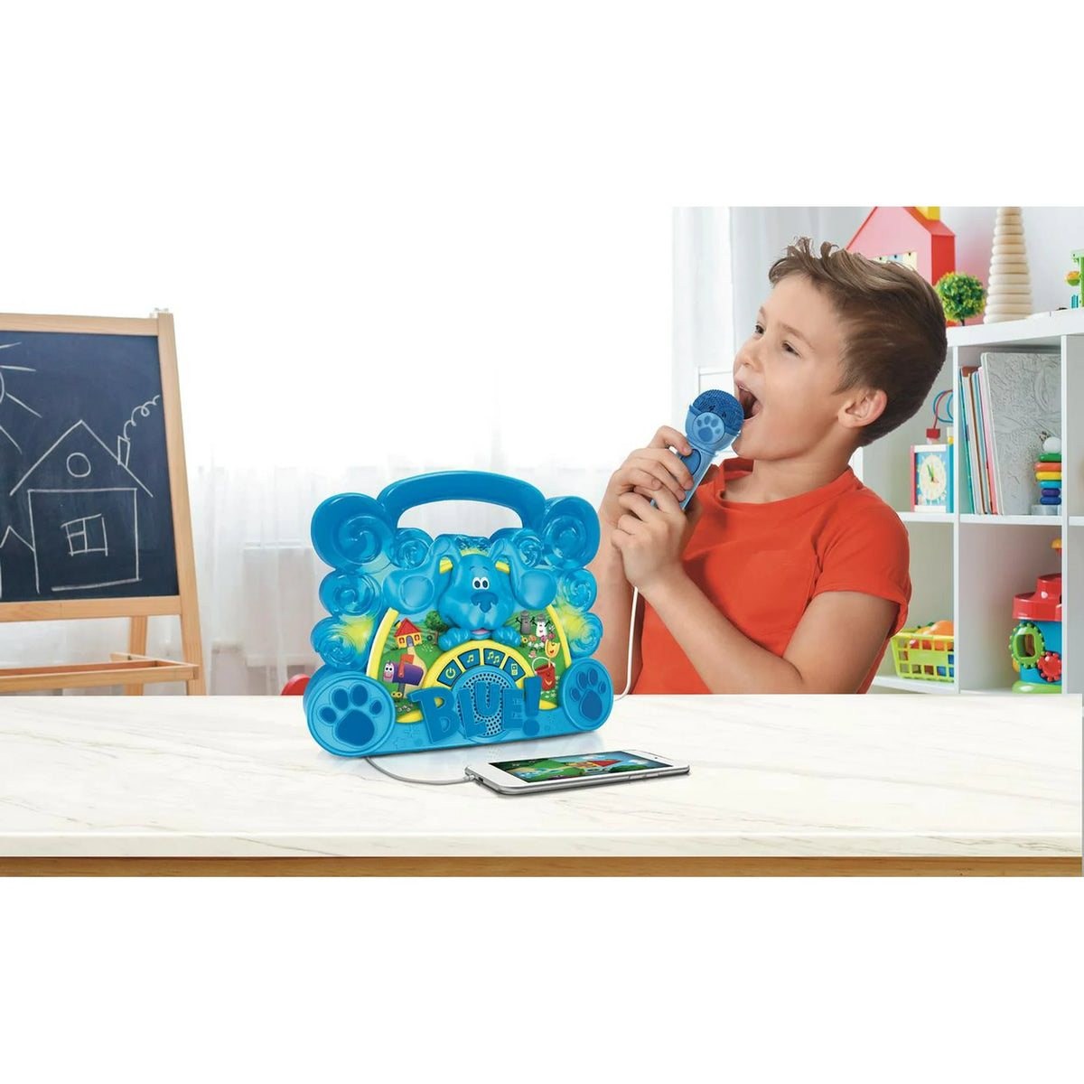 Boy singing into a blue microphone beside a blue puppy boombox connected to a phone