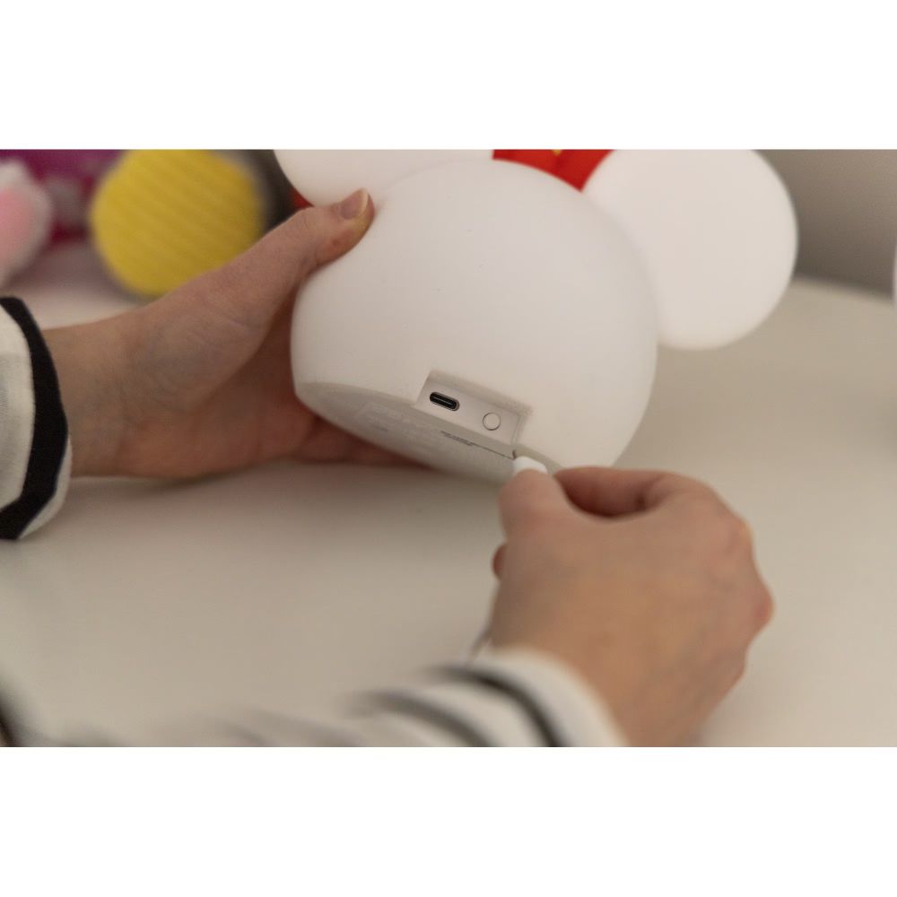 Hand plugging a USB-C cable into the back of the Minnie Mouse lamp