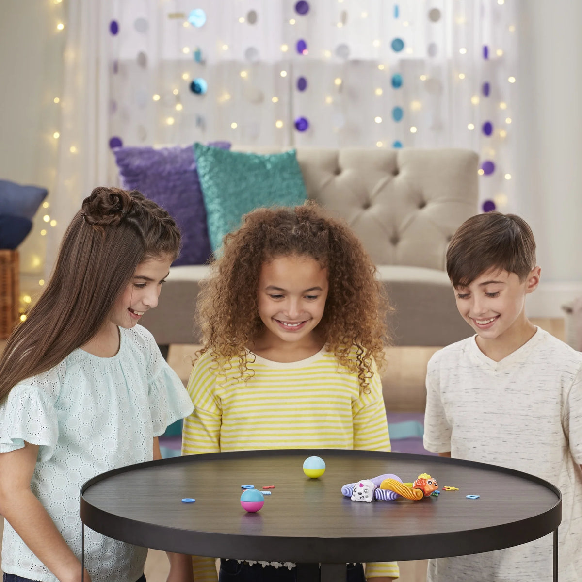 Three smiling kids watching spring animal toys and balls zoom across a round table
