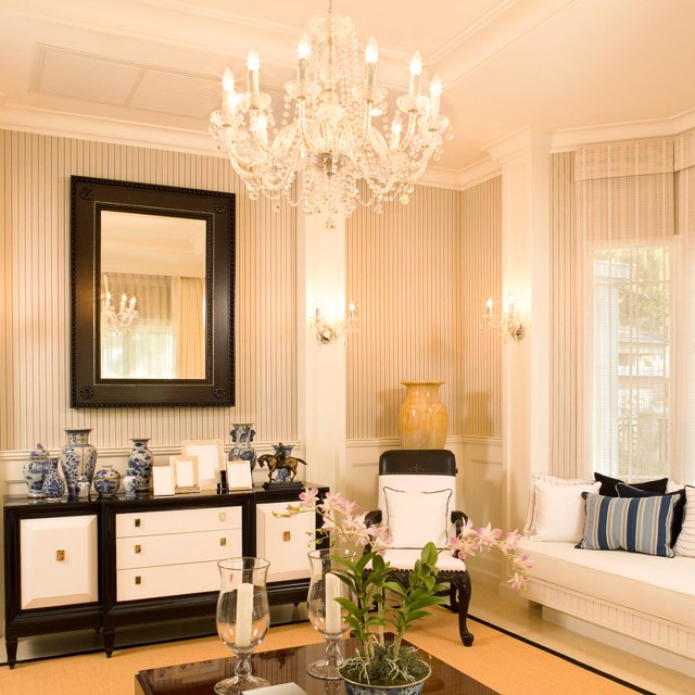 Crystal chandelier and wall sconces lit in a striped wallpaper sitting room
