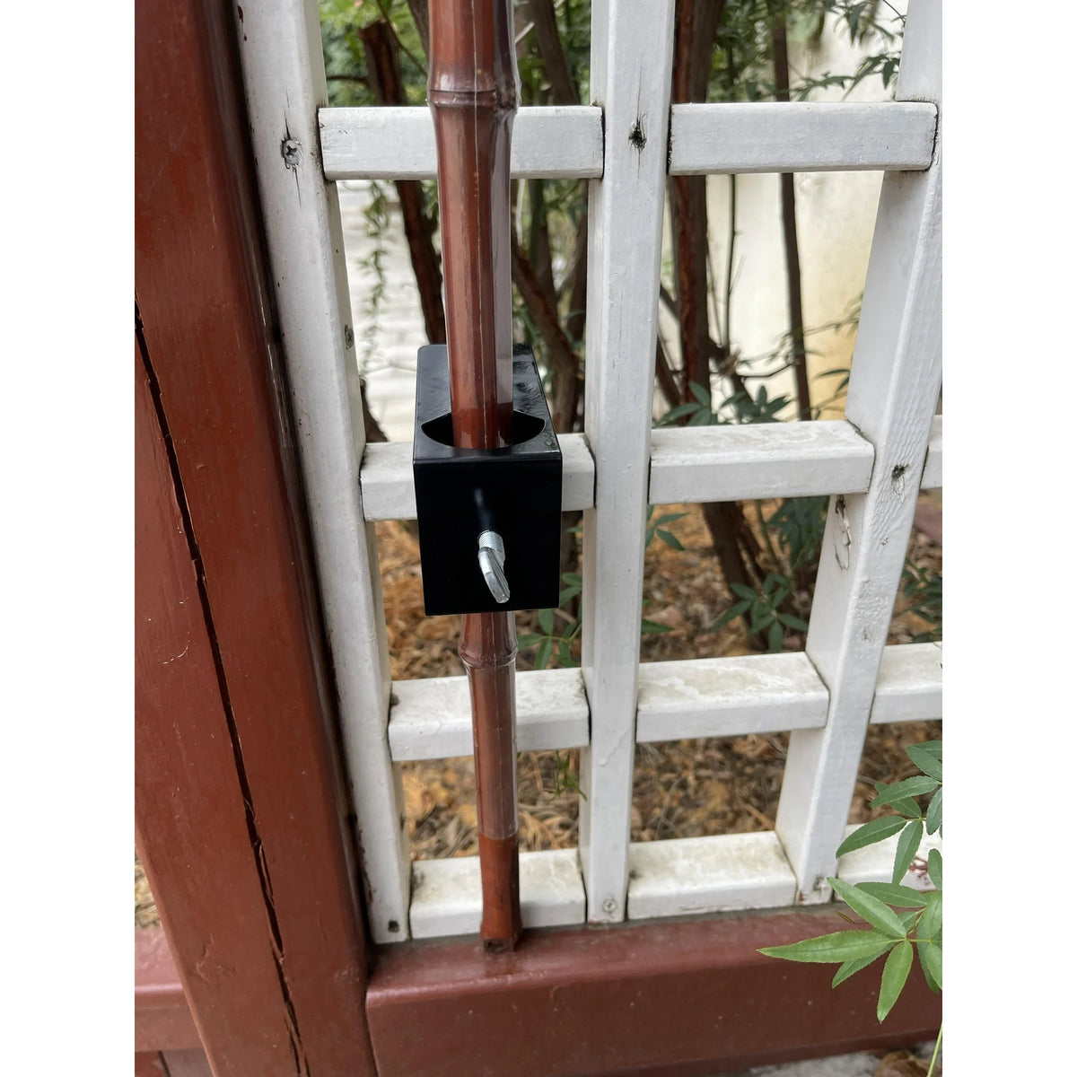 Black deck clamp holding a bamboo pole against a white garden trellis