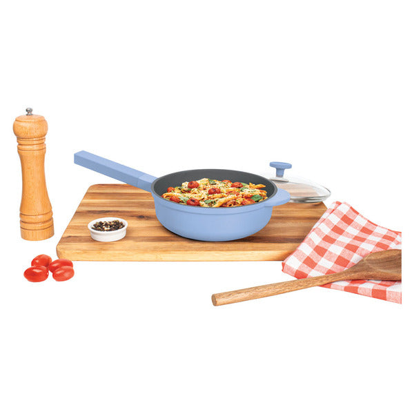Blue 8 inch pan filled with pasta on a wooden board, glass lid, pepper mill and checked towel beside it