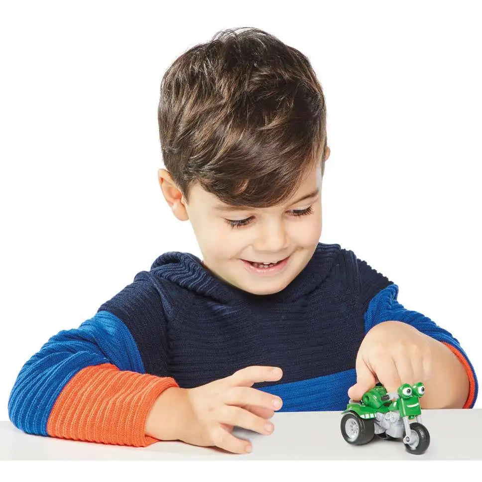 Smiling boy pushing the small green three-wheeled bike toy across a table