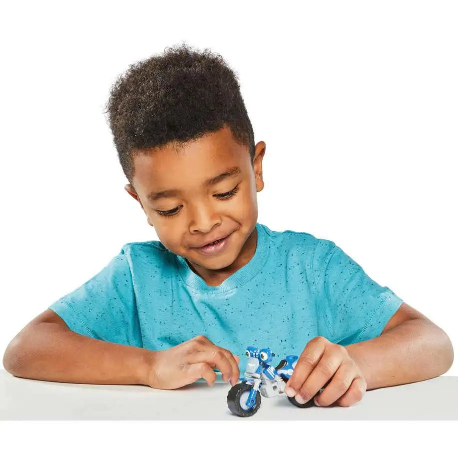 Smiling boy rolling the small blue motorbike toy on a table