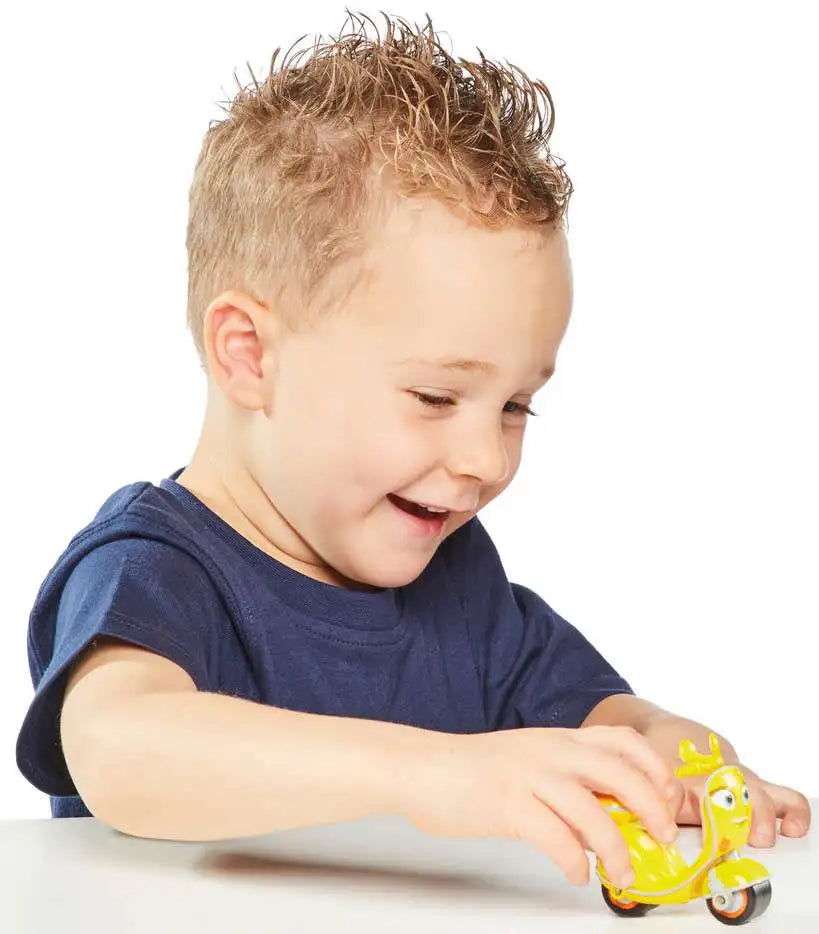 Laughing boy pushing the yellow scooter toy along a table