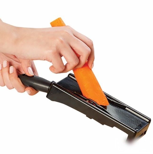 Hand sliding a carrot across the black slicer frame with the peeler clipped in