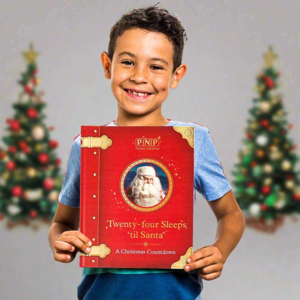 Smiling boy holding up the red Santa countdown storybook between two Christmas trees