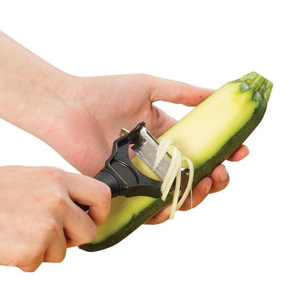Hands pulling the julienne blade along a courgette, making thin strips