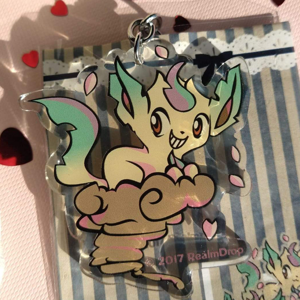 Grinning Leafeon riding a brown tornado cloud acrylic keychain with pink petals
