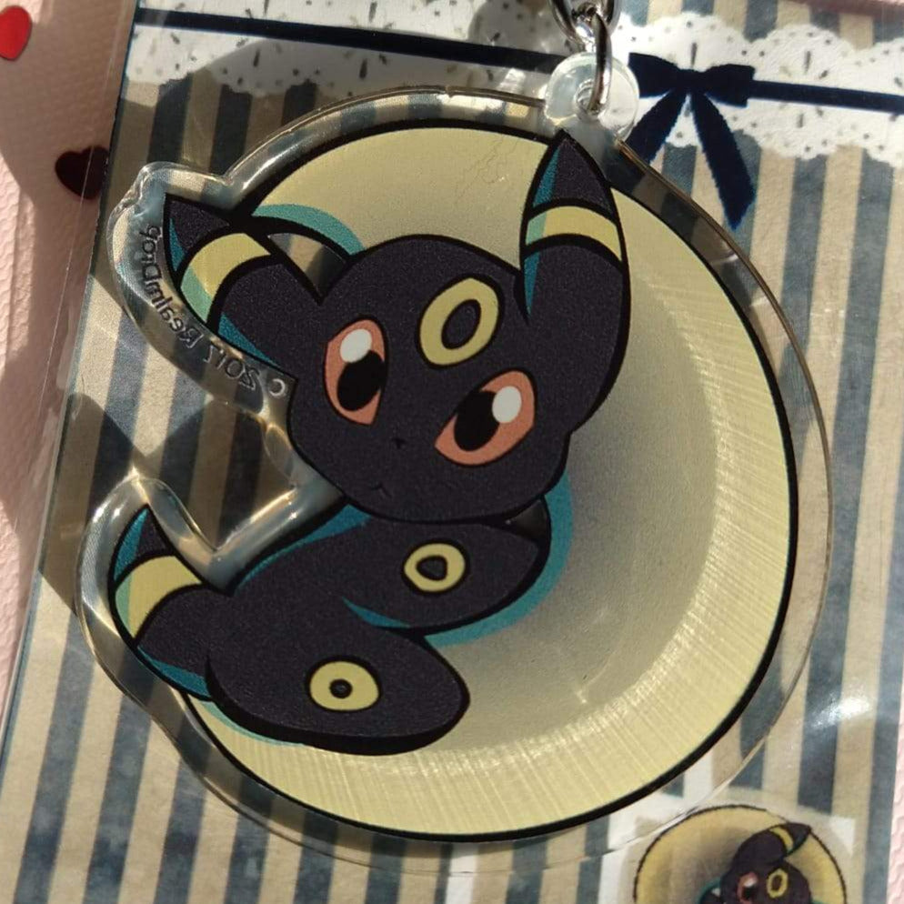 Umbreon resting in a yellow crescent moon acrylic keychain, on its striped card