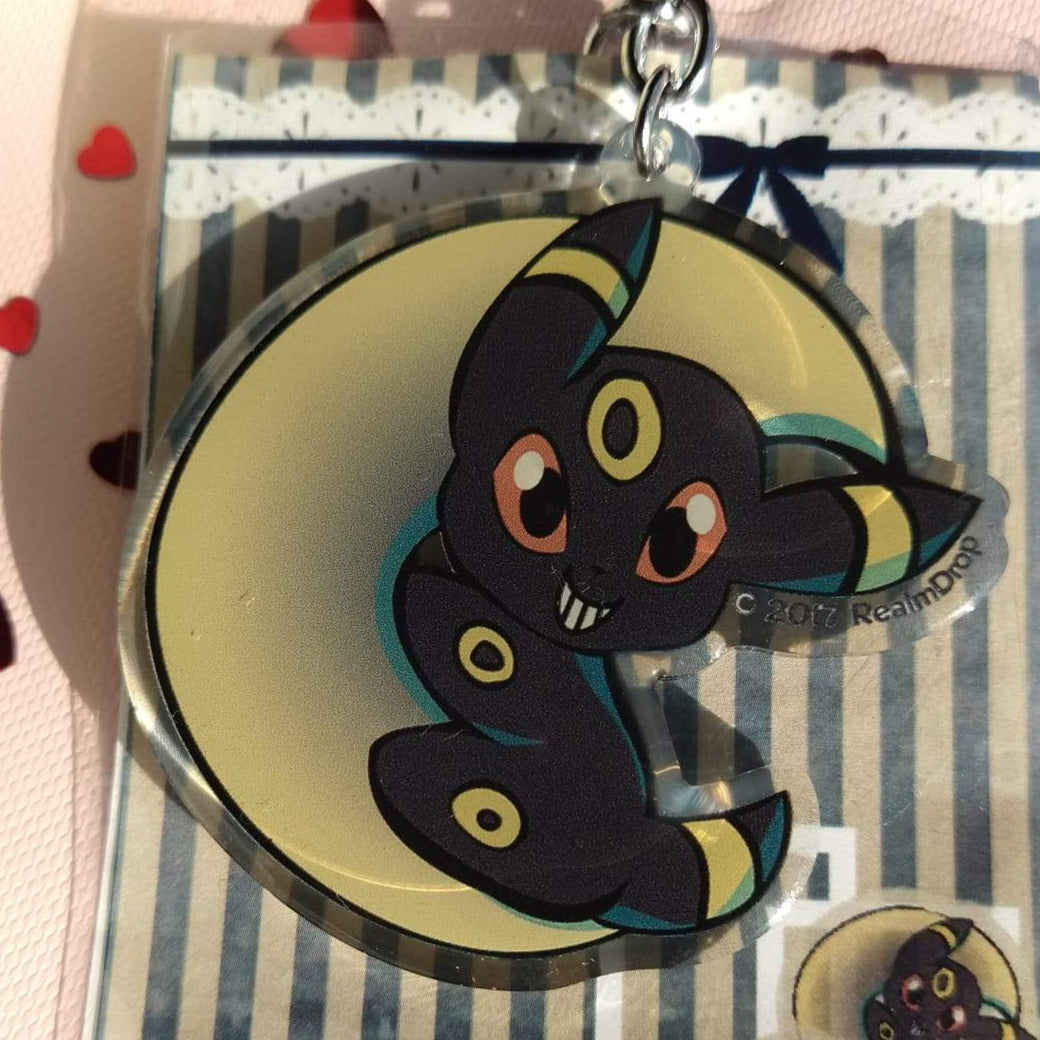 Acrylic Umbreon keychain curled around a pale yellow crescent moon, grinning