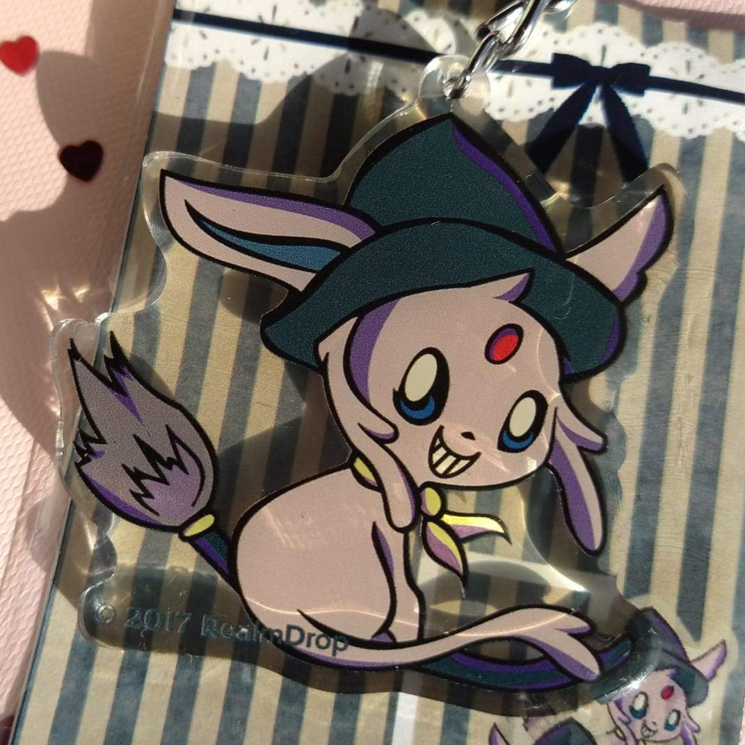 Grinning Espeon in a witch hat on a lavender broomstick acrylic keychain