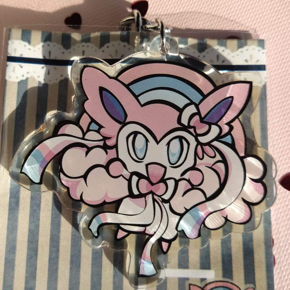 Acrylic Sylveon keychain with ribbon feelers on pink clouds under a pastel rainbow