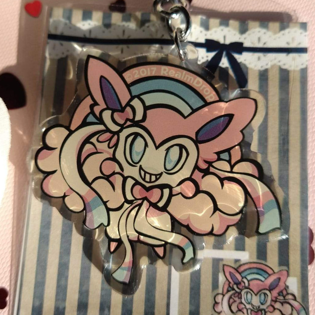 Grinning Sylveon on pastel clouds under a rainbow acrylic keychain