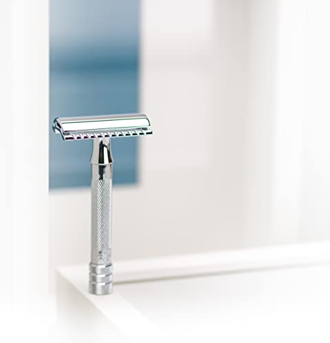 Chrome safety razor standing upright on a white bathroom shelf