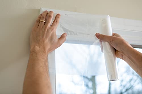 Hands rolling clear insulation film across the top of a window