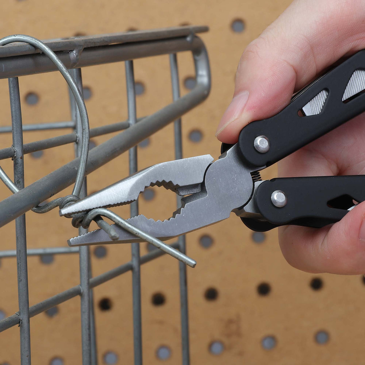 Black multi-tool pliers twisting wire on a metal wire rack