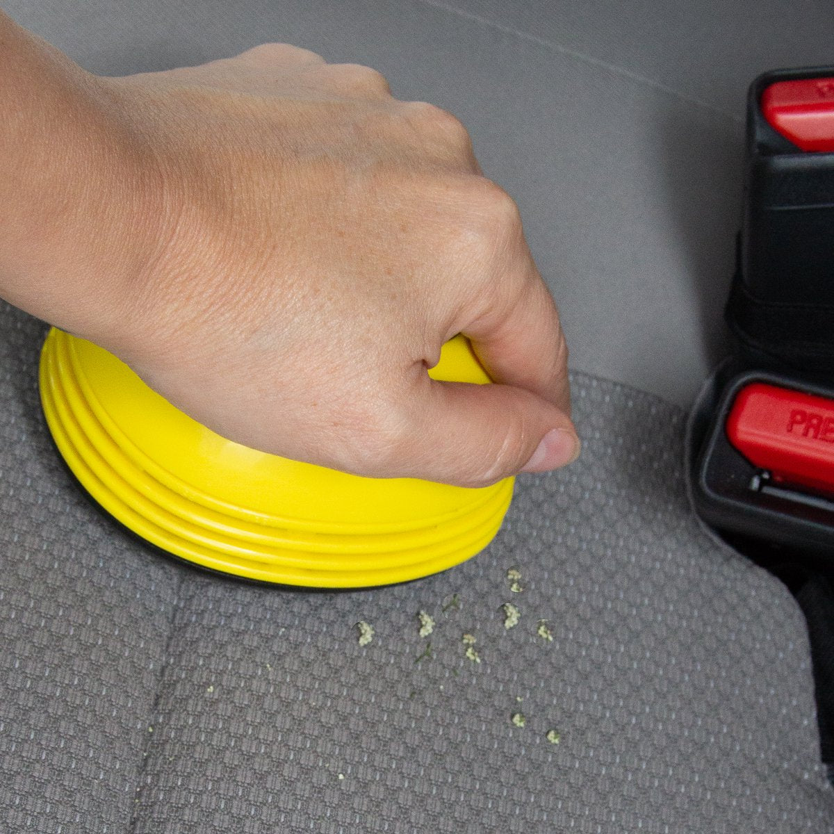 Hand using the yellow mini vacuum to pick up crumbs on a car seat