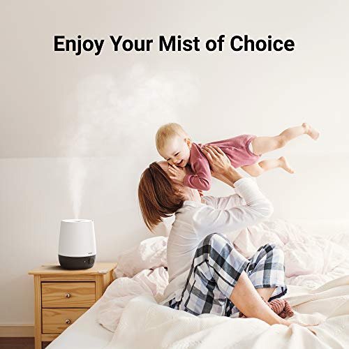 Humidifier misting on a nightstand while a mother lifts her baby on the bed