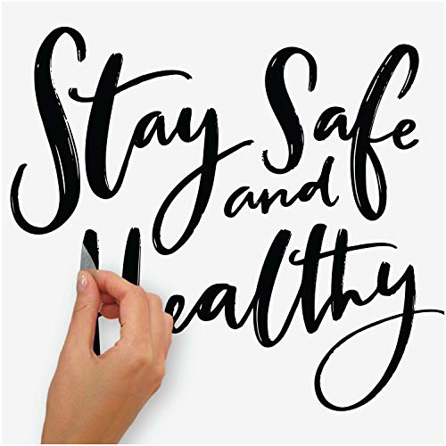 Hand peeling a black script letter of the Stay Safe and Healthy decal onto a wall