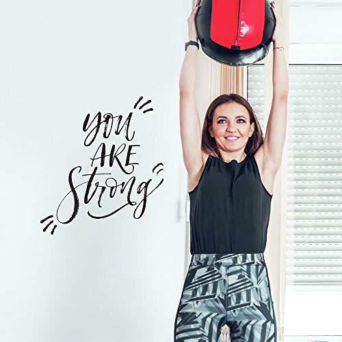 Woman lifting a red medicine ball beside a You Are Strong wall decal