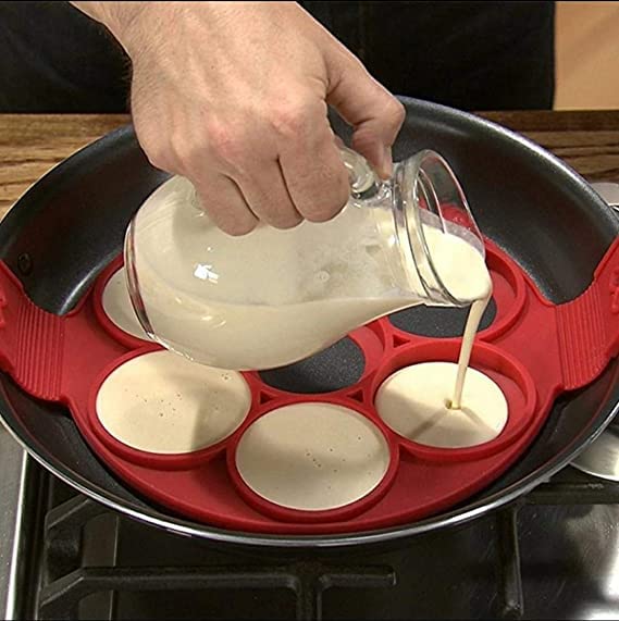 Batter poured from a glass jug into a red seven-ring pancake mould in a pan