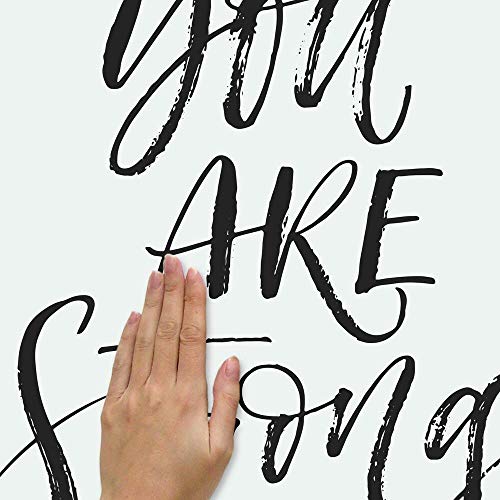 Hand smoothing the black You Are Strong script decal onto a wall