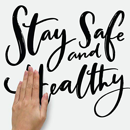 Hand pressing the black Stay Safe and Healthy script decal flat onto a wall