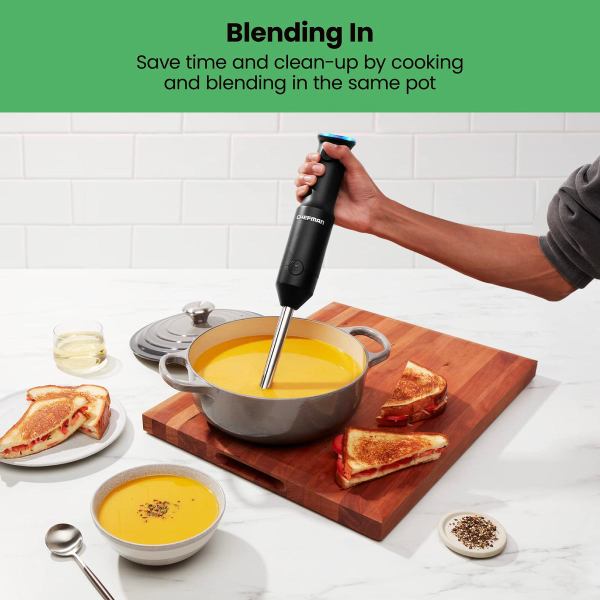 Hand blending orange soup in a grey pot beside grilled cheese sandwiches