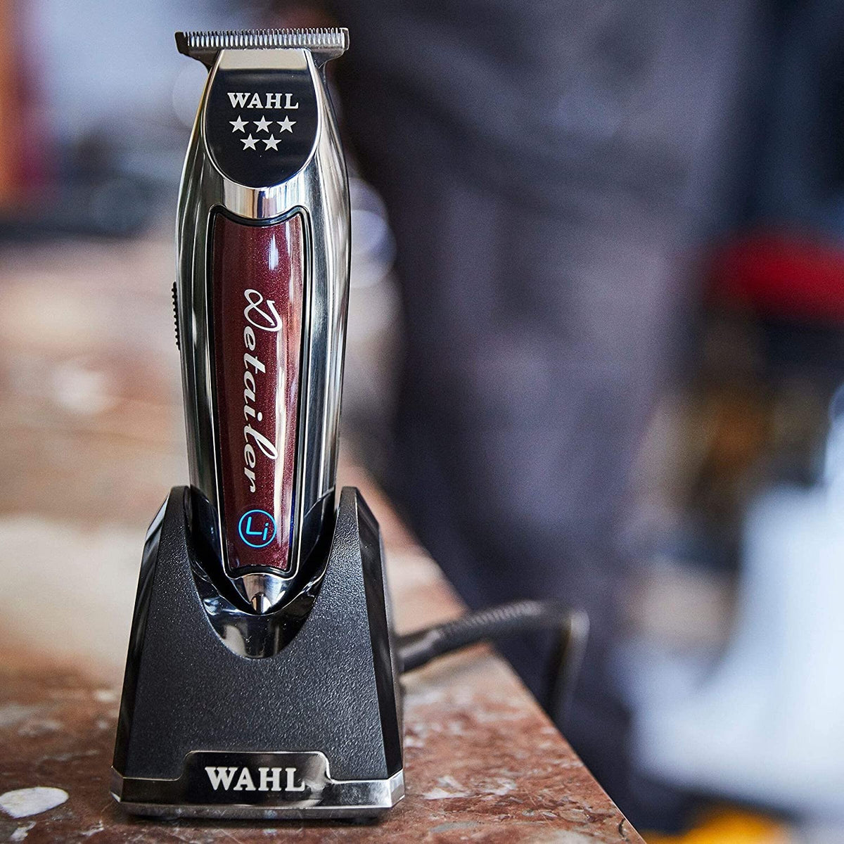 Burgundy and chrome detailer trimmer charging upright on its black stand in a barbershop