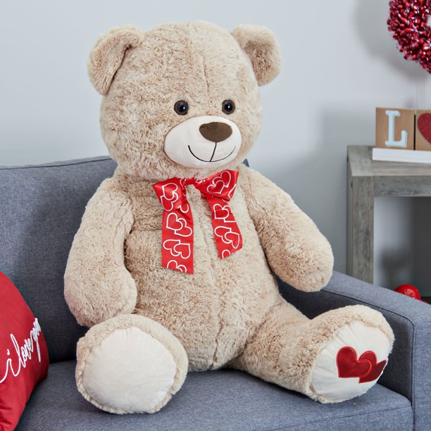 Tan Valentine's teddy bear sitting on a grey sofa with a heart bow