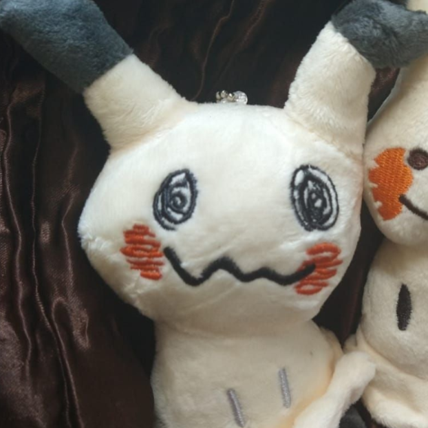 Close-up of a Mimikyu keychain plush with swirly eyes and a zigzag smile